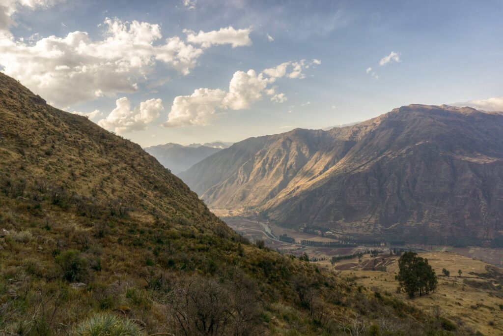 A wide Andean valley falls away between steep ridges under heaped white cloud.